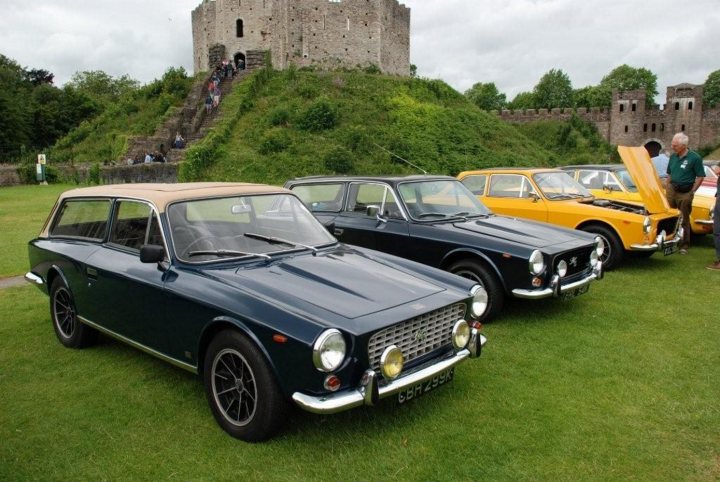 Sixties Pistonheads Estate Quickest - The image captures an idyllic scene of vintage cars parked under the shadow of an imposing castle on a grassy hill. Four distinctive cars, each a different color, sit gleamingly in the foreground. The cars, a stunning deep blue, a vibrant yellow, a regal black, and a sleek silver, seem to be in excellent condition, reflecting the quality of preservation and maintenance that their owners have invested in them. The castle in the background, its stone structure cloaked in lush green trees, provides a striking contrast to the shiny metallic bodies of the cars. The setting evokes a sense of history, as well as adventure, inviting viewers to imagine the stories these classic cars could tell.