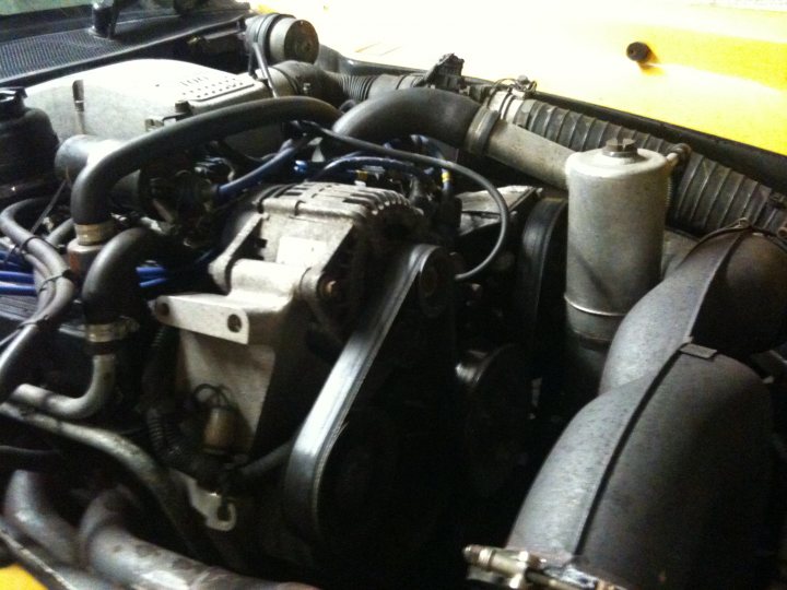 Belt Timing Pistonheads - The image showcases the under-the-hood view of a car's engine, revealing the complexity of the machine with visible gears and hoses. Multiple other parts, straps, and wires are scattered throughout the scene, illustrating the dense packing of elements within the engine compartment. The hoses and pipes run across different levels, demonstrating the comprehensive connections within the vehicle. The overall scene suggests a mechanical intensity typical of an engine bay, where various components coexist to ensure the car's functionality.