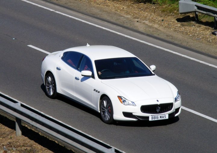 Herts, Beds, Bucks & Cambs Spotted - Page 453 - Herts, Beds, Bucks & Cambs - PistonHeads - The image showcases a white luxury car on a highway, positioned on the right side of the road. It's daylight, and the car is in motion, as indicated by its smooth trajectory on the tarmac. The vehicle is of a twin-turbocharged V12 engine, an Maserati Bergman Maserati, as suggested by the license plate. A guardrail is visible on the left side of the road, providing a sense of scale for the vehicle.