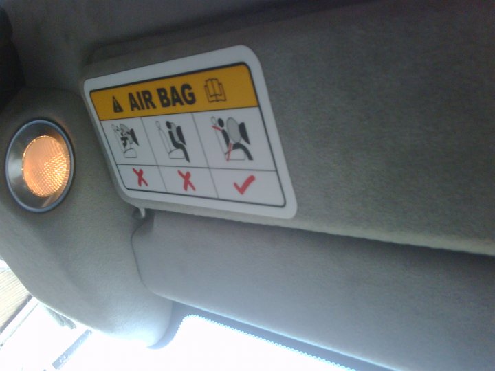 Remove Pistonheads Idea - This image features an in-car seatbelt warning label, commonly known as an airbag warning sticker. The sticker is rectangular with a white background and contains graphic illustrations representing a person seated behind the steering wheel, along with separate symbols for a child and a sleeping or seated rear passenger. Each symbol is followed by a red X indicating that the seat is not equipped to be used by any of these users when the airbag is in operation.