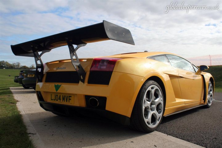 Sunday Service Supply Silverstone Pistonheads Snaps - The image features a vibrant yellow sports car parked on what appears to be a concrete surface, possibly a parking lot. It's an elegant and sleek vehicle, with a prominent rear wing and a distinctive plate number. The sky is partly cloudy and provides a beautiful backdrop for the car. There's a serene feeling in the image, suggesting a calm and quiet setting.