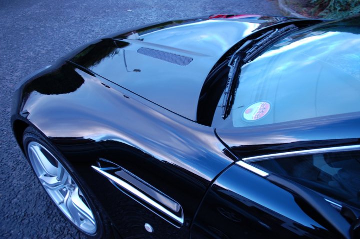 Pistonheads - The image showcases a close-up view of a stylish black sports car, parked on the left side of the road. The reflective surface of the car gleams under the light, highlighting its aerodynamic design. Two small logos are visible, one located on the driver's side, possibly indicating the brand of the car. The car is parked under clear skies, suggesting a sunny day. The overall scene is one of modern luxury and sporty elegance, set against the backdrop of an outdoor roadway.