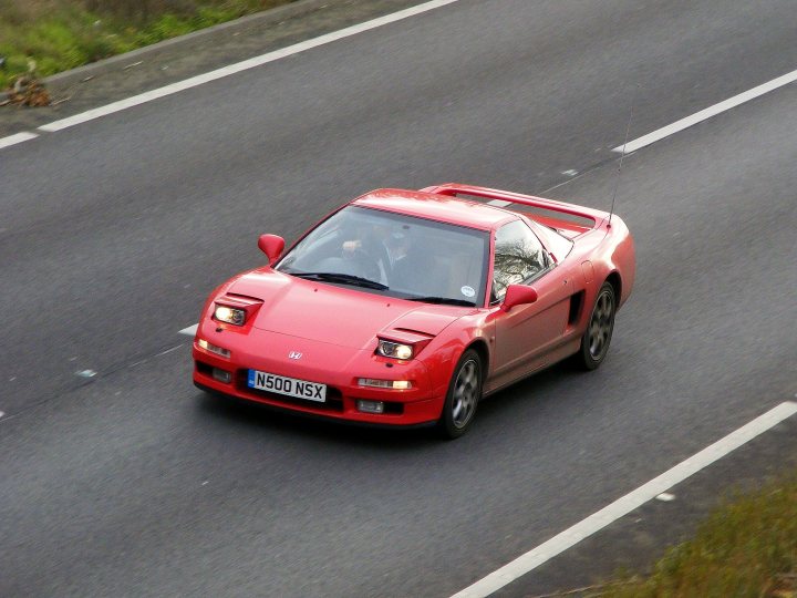 Herts, Beds, Bucks & Cambs Spotted - Page 306 - Herts, Beds, Bucks & Cambs - PistonHeads - The image shows a vibrant red sports car driving down the right side of a road with rural scenery visible on the left. The car's design is sleek and low-profile, indicative of high-performance vehicles. The sun appears to be low in the sky, casting its glow on the scene, enhancing the colors, and produces lens flare. The license plate on the car reads "N500 NGX" and there's a distinctive shape in the front bumper, likely part of the car's design. The overall style of the vehicle and the road setting suggest that this image might be a stock photo.