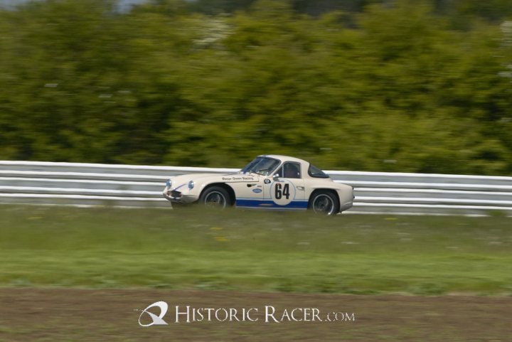 Early TVR Pictures - Page 4 - Classics - PistonHeads - The image shows a vintage silver race car numbered 46 racing swiftly on what appears to be a race track. The vehicle is positioned to the left side of the frame, emphasizing its movement through sharp cornering. The background is filled with a verdant landscape of trees, suggesting the track is set in a lush, green environment. The watermarks of "HistoricRacer.com" indicate that this is a photograph taken from the perspective of someone watching the race from the sidelines.