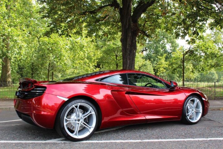 Advice Please - Page 1 - McLaren - PistonHeads - The image showcases a vibrant red Audi sports car parked in daylight on a street. The car's sleek design and shiny finish reflect the sunlight and the trees lining the pavement in the background. Directly behind the car, there's a tree with lush green foliage, adding a natural contrast to the sleekness of the vehicle. A fence is partially visible further down the street, suggesting a residential or park setting. The overall scene is serene, with the sports car as the focal point.