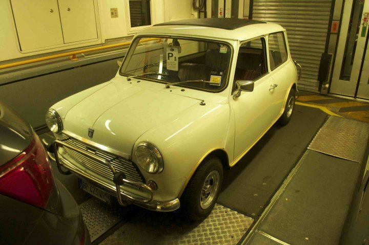 Returning after 38 years! - Page 1 - Classic Minis - PistonHeads - The image showcases a perfect scene at a car dealership. Dominating the frame is a pristine white Mini Cooper, its vibrant hue gleaming against the backdrop of the dealership. The car is neatly parked on a ramp positioned just right to display it for potential buyers. 

Adding to the charm, the Mini Cooper sports a black roof rack, standing out against its white exterior. The ramp's placement and the car's proud posture suggest it's ready for its next test drive. 

The dealership itself looks clean and professional, with white walls that contrast sharply with the car's white exterior, thereby drawing attention to the vehicle. The overall image paints a picture of a well-organized and inviting car dealership.