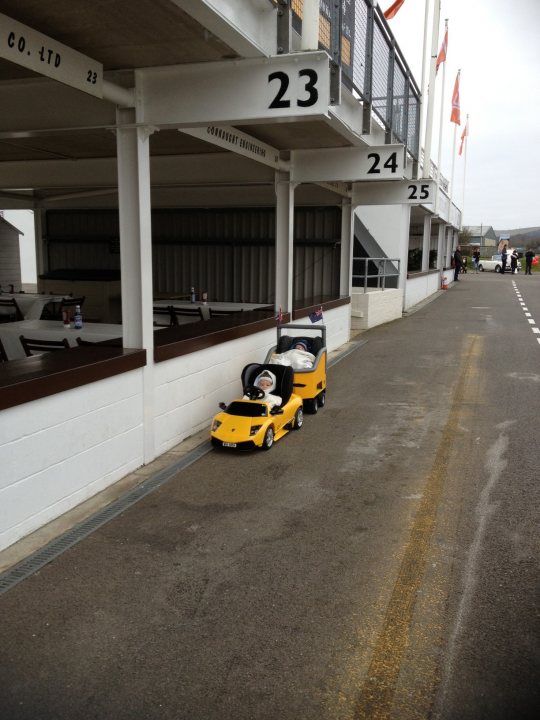 Breakfast Club 2013 - Page 3 - Goodwood Events - PistonHeads - The image showcases a playful scene in a garage or parking lot, where there are two toy cars carefully positioned. One toy car is yellow and is located on the right side of the image, while the other is white and is situated on the left. The buildings in the background have a numbering system, with 23 and 24 prominently displayed, possibly indicating the doors or spaces where these toy cars were left.