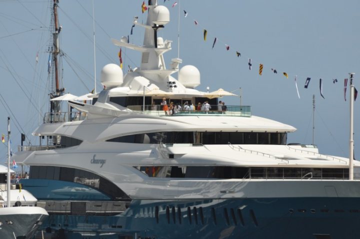 Celebrating 20 years of ... - Page 1 - Vipers - PistonHeads - The image showcases a large, white superyacht docked at what appears to be a harbor. People are visible on the upper deck of the yacht, enjoying the view or preparing for an event. The sky above is clear, suggesting good weather. In the background, a cluster of smaller boats is visible, adding depth to the scene. From this perspective, the yacht seems to shade the vessels behind it, allowing them to appear partially obscured. The image gives a sense of the scale and grandeur of the superyacht compared to the other boats.