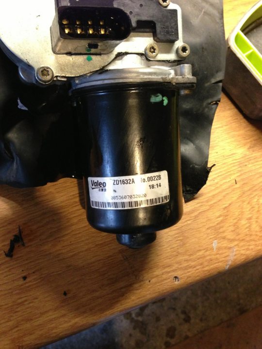 A blender sitting on top of a counter - Pistonheads - The image displays a mechanical component with a black housing, partially assembled on a wooden surface. A black cover is adhered with what appears to be glue or adhesive, exposing the metal internal parts of the component. On the component, there is a white label with black text providing information about the part. Around the base of the component, there are several metal screws and holes into which they would be inserted. The presence of a green mark on one part of the component suggests it may have been identified, perhaps for servicing or repair.