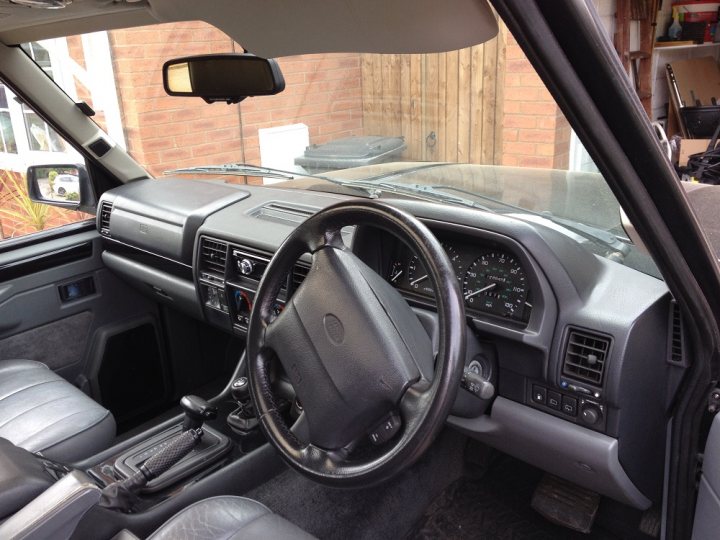 Range Rover classic - Page 18 - Land Rover - PistonHeads - The image shows the interior of an SUV viewed from the passenger side. The photo centers on the dashboard and steering wheel, providing viewers with a partial sightline into the vehicle's interior. The steering wheel, which is leather-wrapped and prominent in the frame, is set against the dashboard that features various gauges and controls. Below the wheel, the gear shifter is visible. The SUV appears to have a driver's side door open, and there are no visible passengers or belongings in the car. The style of the vehicle's interior suggests a practical and durable design, typical for SUVs.