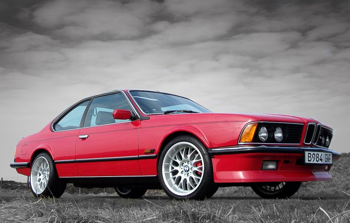 Tatton Park Pistonheads Classic - The image showcases a red BMW car positioned on a grassy surface. The car is oriented to the right, dominating a large portion of the frame. The BMW has a classic design, characterized by a long hood and a short tail. It features white wheels that contrast with the red body. The sky forms the backdrop of the scene, adding a dynamic contrast to the static vehicle. The overall atmosphere exudes a sense of tranquility with the car being the primary focus against the natural setting.