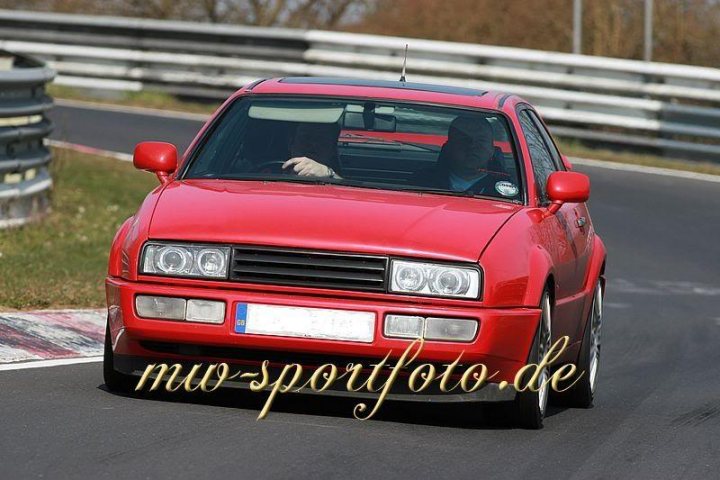 Corrado Sotw Pistonheads - The image features a vibrant red sports car with a black soft top top approaching the camera, seemingly head-on on a road. It has a striking design with four doors and alloy wheels. The car exhibits the sleek lines characteristic of sports cars. The photo captures the car against a blurred backdrop, emphasizing speed and motion.