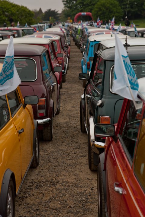 London to Brighton  - Page 1 - Classic Minis - PistonHeads - The image presents a group of vintage cars parked in a row on a dirt road. The cars are predominantly colored in shades of maroon, green, and white. They feature a classic style with rounded bodies and smaller wheels. The vehicles display license plates, indicating that they are registered for use on public roads. The sheer number of cars suggests that this might be a special event or gathering related to vintage or classic vehicles.