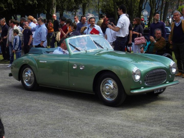 Deste Villa Concoursporn Pistonheads - The image showcases a classic green car driving through a crowd of people. The car appears to be a vintage or classic model, judging by its distinctive design and color. There are several individuals standing on the pavement to the side of the car, appearing to watch the car pass by. Some of them carry handbags and one person is smoking a cigarette. The setting seems to be a public outdoor area, possibly a street or a park. The atmosphere seems to be calm, with everyone seeming to go about their day.