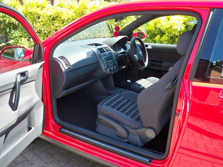 Gti Polo Pistonheads - The image showcases the interior of a red car, with a focus on the driver's side area. The car features a black steering wheel centered on a dashboard, equipped with a radio system. Below the dashboard, you can see the front passenger seat, which is covered by a gray headrest with a checkered pattern. The image also captures the right side door, where there is a clear reflection of the car and its surroundings on its surface.