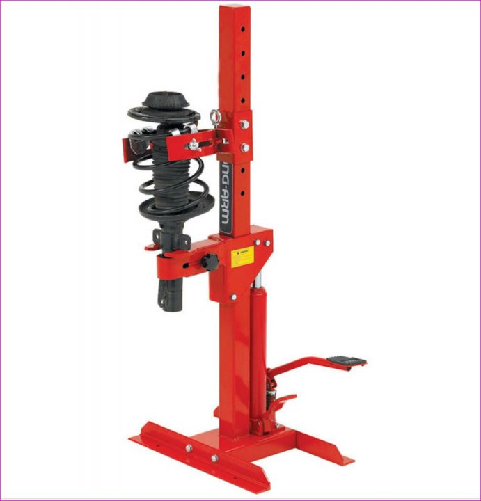 are MK1 and MK2 springs the same? - Page 1 - Mazda MX5/Eunos/Miata - PistonHeads - The image displays a piece of industrial or mechanical equipment, which appears to be a straddle press unit, likely used for compression or testing. It has a red frame and includes a vertical section, a circular guide on top, and a lever on the side. The equipment is mounted on a base plate with upright supports, suggesting it is designed to take vertical forces. The background is a solid, plain white, emphasizing the equipment without any distractions.