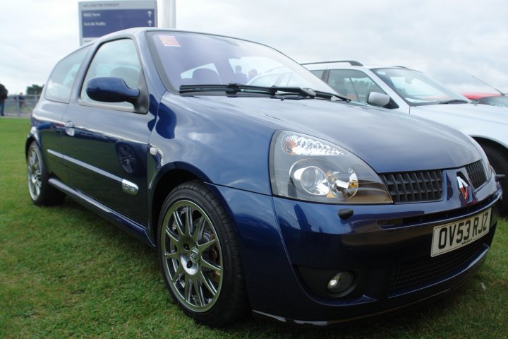 A white car parked in a parking lot - Pistonheads - The image displays a blue hatchback car parked on a grassy area. The car is equipped with alloy wheels and a sunroof. The vehicle is positioned in front of another car whose back is visible, suggesting a perspective taken from behind the first car. The sky is overcast, and there are no visible texts or logos on the cars. The style of the image suggests it was taken in broad daylight, and the focus is on the cars and their details.