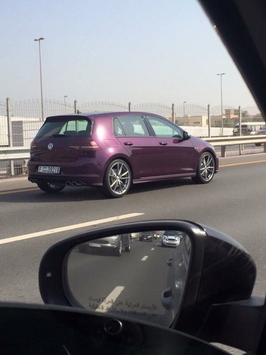 Post pictures of your Golf R here - Page 2 - Audi, VW, Seat & Skoda - PistonHeads - This is a photograph taken from inside a vehicle displaying a rear-view mirror. The mirror reflects a curved road where a purple-colored sedan is in motion. The car stands out with its shiny paint job. Beyond the car, there's a blurred background with fencing beside the road, suggesting a journey through an urban or suburban area, possibly towards industrial or commercial zones along the horizon.