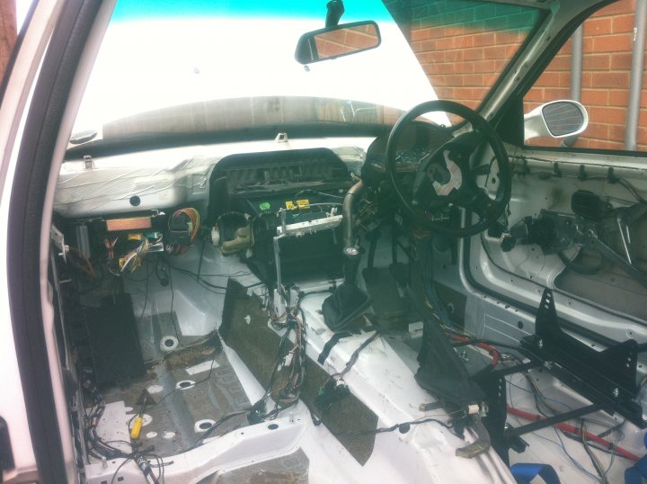 Pistonheads - The image shows an interior view of a vehicle. It appears to be an older car with a partially upholstered interior, missing doors, and exposed wiring and mechanical components. The steering wheel is visible, along with other controls that are commonly found in a vehicle's dashboard area. There is no upholstery visible, exposing the skeletal structure of the car's interior. The background outside the vehicle's frame shows part of a brick wall, indicating that the car might be parked on or near the pavement.