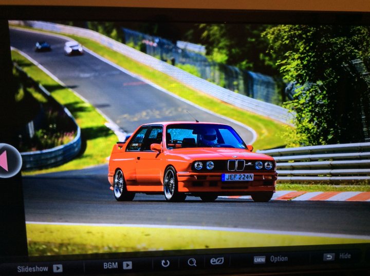 E30 M3 prices - Page 10 - M Power - PistonHeads - The image captures a dynamic scene on a race track, featuring an eye-catching red BMW car in the middle of the frame, moving at high speed. The car's number, 227, is prominently displayed on the hood and the rear wing. The track appears curved, as indicated by the camera's angle and the positioning of the car. There are two other smaller cars visible in the background. The entire scene conveys the thrill of a high-speed race.