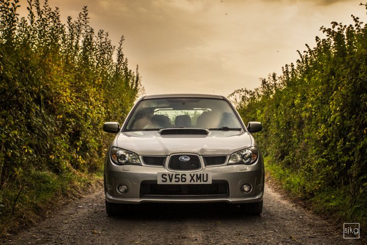 Show off your Subaru!! - Page 63 - Subaru - PistonHeads - The image shows a silver SUV traveling on a narrow, dirt road that is bordered by hedges or bushes with green leaves. The sky is overcast, and the daylight appears faded, suggesting either dawn, dusk, or a cloudy day. The vehicle's license plate is visible and reads "SV56 XUM." The photograph has a candid style, capturing a moment as the car moves forward. The overall atmosphere of the image is serene and somewhat naturalistic.