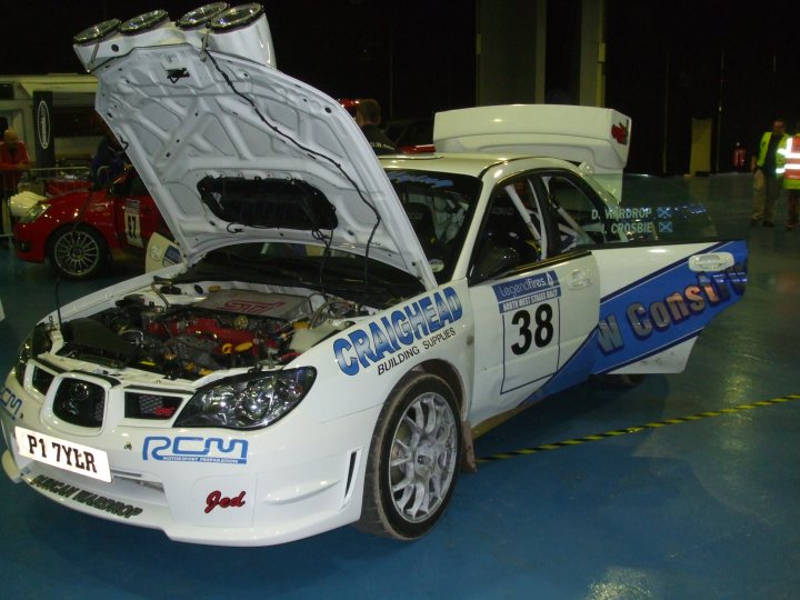 Weekend Stages Pistonheads - In the image, a white sports car is parked on a blue concrete surface within a building. The car has an extravagant hood adorned with custom graphics and is part of a motor show, given the context. The driver-side door is slightly ajar, revealing a sports seat equipped with a harness, hinting at the car's racing capabilities. The vehicle features a license plate at the rear. The ambiance inside the building seems to reflect the excitement and prestige associated with such an event.