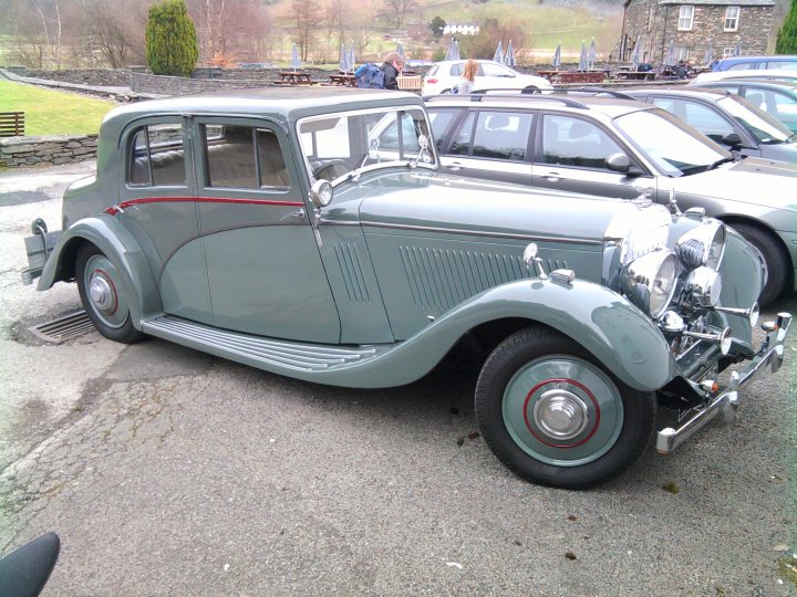 Saw this today... - Page 1 - Classic Cars and Yesterday's Heroes - PistonHeads - The image features an old-fashioned car parked on what appears to be an asphalt surface, possibly a parking lot. The vehicle has a classic design, with a sleek green body, curved lines, and a prominent chrome grille. It is a four-door car with a visible trunk area in the back. The wheel rims have a distinctive red and white stripe design, and there are two side mirrors.

The car is one of several vintage vehicles on display. In the background, there are other old-fashioned cars, though the focus is on this particular gray vehicle. The setting is outdoors during the daytime with no specific landmarks or buildings to identify the location. There are no distinguishing features or signs in the immediate vicinity that would provide additional context. The overall atmosphere is calm and somewhat nostalgic, evoking a sense of the past.