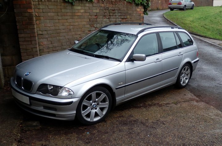 TerraClean -Just had it done + air filter + vortex breather. - Page 1 - BMW General - PistonHeads - The image showcases a shiny, gray BMW car parked on a road, on what appears to be a rainy day. The car is positioned facing the camera, with its sleek design and distinctive BMW badge visible on the grille. Around the vehicle and on the ground, there are puddles, suggesting recent rainfall. The car is situated on the left side of the road, with the side mirror area gleaming. A building with a red brick wall can be seen in the background, adding a touch of urban residential setting.