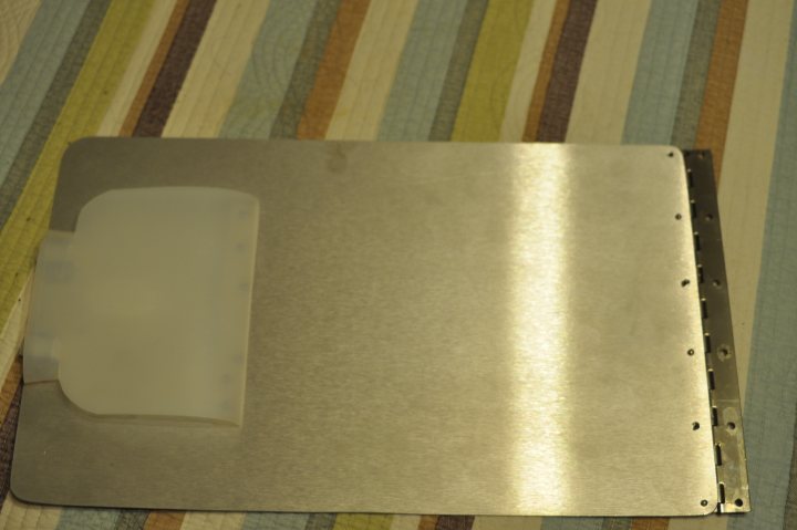 Pistonheads - The image presents a close-up view of a flat, metallic object, which appears to be a sliver or silver plate. This object has a backing with a series of holes, suggesting it's an electric component or a pedal, likely used in an electronic device or musical setup. The object has a reflective surface, indicating it might be made of tin or another reflective metal. It's placed on a surface, perhaps a table or ground, as it's resting on a blue and green patterned surface. The surrounding ambient light gives the object a silvery hue that catches the light, emphasizing its metallic nature.