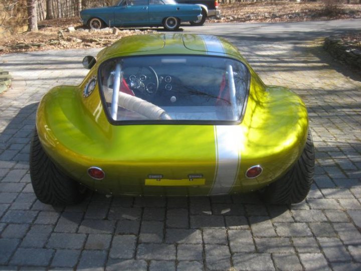 Bill Thomas Cheetah - Page 1 - General Gassing - PistonHeads - The image features a vibrant, two-tone yellow car resting on a paved surface. The car's design, resembling an early Volkswagen Beetle, is notable with a small notch at its front and a rounded rear. An iconic feature of this vehicle is the large, wrap-around windshield that wraps around the entire creation. In the background, partially visible, is another vehicle, a classic blue car seemingly parked in the vicinity, adding a contrasting color to the scene.