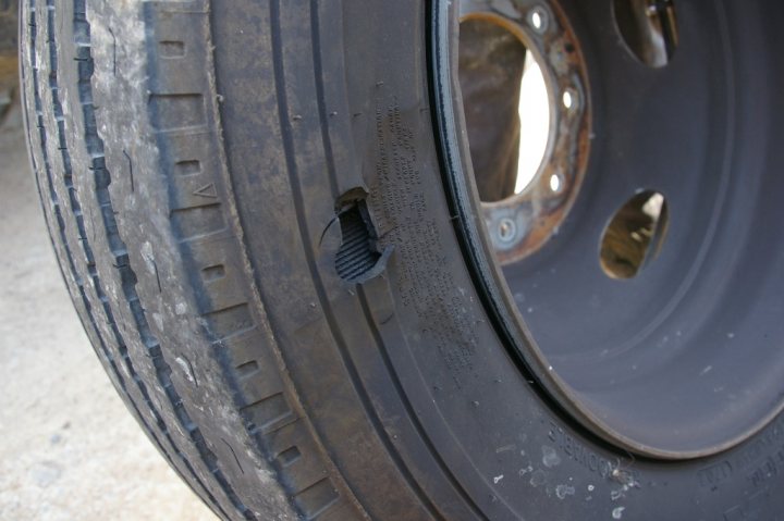 Old tyres - Page 1 - Tents, Caravans & Motorhomes - PistonHeads - The image displays a close-up view of the inside of a wheel for a vehicle, specifically showcasing the lug nut area on a black tire. A lug nut is visibly missing, causing a immediate and significant safety concern. The tire itself appears to be in poor condition due to its natural aging and potential for further deterioration. The inside grooves of the wheel can be seen, suggesting it might not be a conventional alloy wheel. The background is blurred, putting the focus on the potential issue at the center of the image.