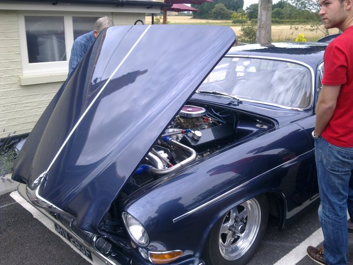 Pistonheads - The image depicts a vintage blue wagon parked in front of a beige building. A person, presumably a man, is standing by the vehicle, looking at the open hood, which is propped up by a prop-stand. The car's engine is on display, suggesting that it may be in the midst of a mechanical operation or undergoing maintenance. The setting is an outdoor area, likely a parking lot, as indicated by the presence of the building and the paving of the ground beneath the car. The atmosphere evokes curiosity and a sense of exploration, perhaps indicating an interest in automotive mechanics or historical models.