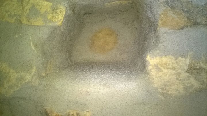 Our French farmhouse build thread. - Page 5 - Homes, Gardens and DIY - PistonHeads - The image shows a close-up view of a stone or stucco surface with a visible light-reflection pattern. The structure appears to be made of masonry or a similar stonework material. Within the textured surface, there is a noticeable circular pattern created by the stone's grain and sanding. This pattern resembles the face of a mask or a celestial body, given the light-dark variations that enhance the illusion. The stone has a weathered appearance, suggesting age or exposure to the elements.