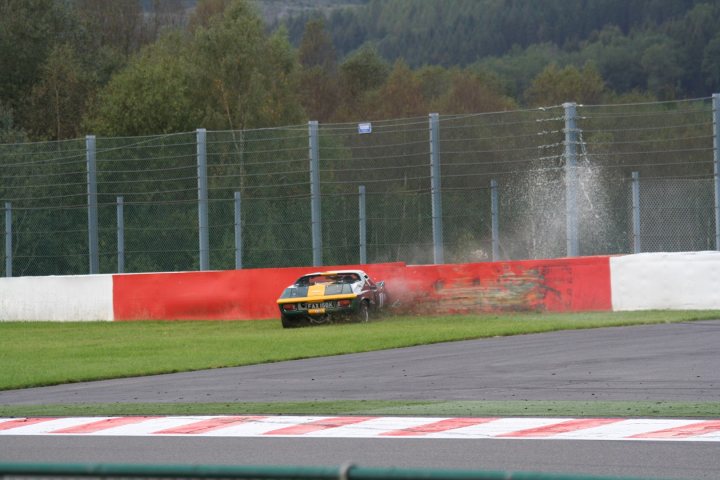 A train traveling down tracks next to a lush green field - Pistonheads - In the image, a vibrant red and white wall is situated at the back of a racetrack. The wall carries a scorch mark from a racing car incident. At the top of the image, a blur of blue sky contrasts with the dark greenery of the forest in the background. In the foreground, the green track seems to tell a silent tale of the crash. The racing car has skidded into the barriers, spraying smoke into the air, leaving a dramatic scene in its wake.