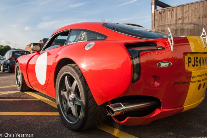 A red and black motorcycle parked in a parking lot - Pistonheads - In the image, a red sports car is seen in a parking lot. The car, characterized by its black and silver rims, is facing towards the right side of the photo. The license plate of the car reads "P J54 W", and the photo also includes a yellow sign in the background. The surrounding environment suggests a typical day at a parking lot with other cars parked in the background.