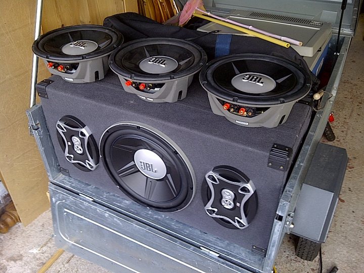 Music in a field - Page 1 - Tents, Caravans & Motorhomes - PistonHeads - The image shows a custom-built car stereo system installed in the trunk of a truck. The stereo system features a powerful 12" subwoofer and two 6.5" speakers, presumably woofers, mounted on a board that is affixed to the trunk floor. The components of the system are organized neatly, and there are visible connectors suggesting a rigorous and robust installation.