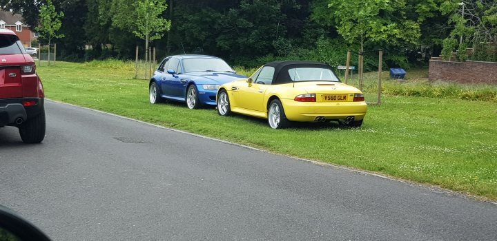 Supercars spotted, some rarities (vol 7) - Page 198 - General Gassing - PistonHeads - This image depicts a scene on a road where several cars are parked. There's a mix of vehicle types, including two sports cars and two other vehicles with different designs. The sports cars are yellow and blue and appear to be in the middle of the road, while the others are situated towards the sides. The street itself is paved, and there are trees lining the road. A few trucks can also be spotted further down the road. The setting suggests a calm day with clear visibility, and the presence of various types of vehicles hints at an urban or suburban environment.