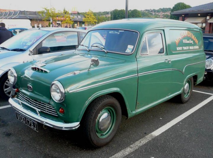 Pistonheads - The image features a **green vintage car** prominently positioned in a parking lot, with other cars visible in the background. The vintage car has a distinctive **Triumph Herald** model, as indicated by the model name written on its side. Its **silver grille** and black roof are additional notable features. Adjacent to the car, there's a **truck** with the words "**Handy Tray Man William Lee Owner**" printed on it, presumably advertising the owner. The overall scene suggests a day at a car parking facility.