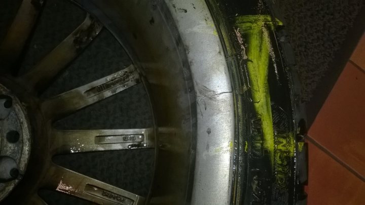 Pistonheads - The image shows a close-up view of a car wheel against a textured backdrop. The wheel appears to have suffered some damage, with the spokes and area close to the vehicle's hub painted yellow to indicate damaged or worn components. The design on the spokes nearest the hub is visible, suggesting the wheel is an alloy model, possibly from a European manufacturer. The surface of the wheel and the part adjacent to it are rusted and corroded, reflecting exposure to the elements. The surrounding area seems to be indoors, with a patterned floor visible and the edge of another wheel or component to the right edge of the frame.