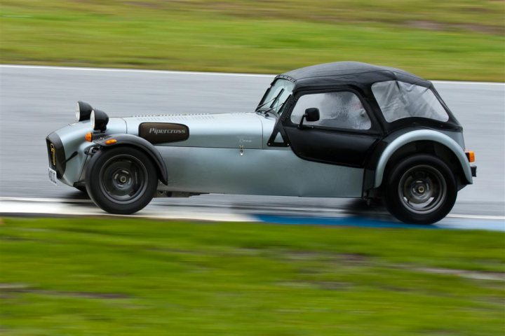 Pistonheads - The image showcases a high-speed chase taking place on a street. The primary focus is a sleek, track-optimized sports car, painted in a striking combination of black and white, with its hood up, indicating it's in full racing mode. The car is sharply angled on what appears to be a curved track, suggesting motion and speed. The blurring effect on the background reinforces the sense of rapid movement.