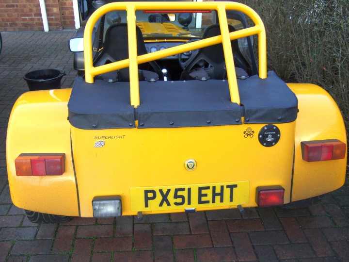 Great day for a blat! - Page 1 - Caterham - PistonHeads - This image showcases the back of a vintage vehicle, specifically an older model convertible. The car is yellow with black detailing, featuring a prominent rear bar and tailgate design. The vehicle is parked on a driveway with a brick surface, and there's foliage visible in the background, suggesting a suburban setting. The license plate includes the letters 'PX51EHT', indicating it could be registered in the United Kingdom where car registration tags often reflect the regions where they are registered.