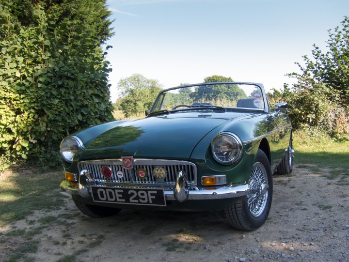 Lets see a picture of your classic(s) - Page 192 - Classic Cars and Yesterday's Heroes - PistonHeads - The image showcases a green classic car parked on a gravel driveway. The car is a two-door vehicle with a visible emblem on the grille, and it's characterized by round headlights. The car is set against a backdrop that includes a grassy field and a line of trees. The sky overhead is blue, indicating a clear day.