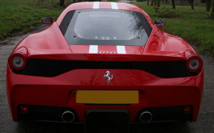 A red and white car with a red bow on it - Pistonheads - The image shows a red Ferrari car parked on a road. The car features a glossy finish, with its hood open, revealing part of its engine. There is a distinctive percentages logo on the side near the back of the vehicle. The setting appears to be a rural or suburban area with greenery and a path visible in the background. The car appears to be in good condition, with no visible damage or wear, suggesting it might be well-maintained.