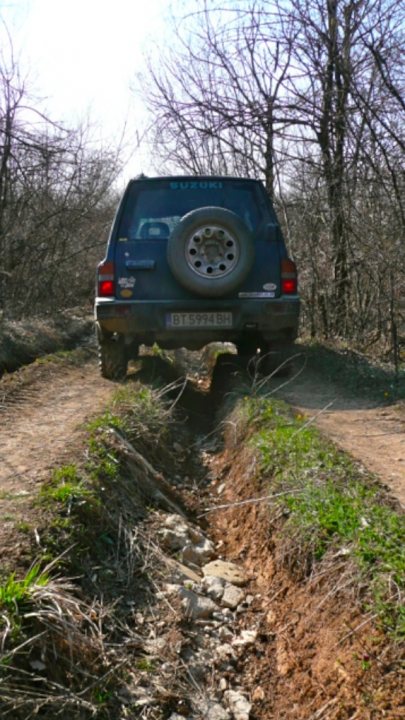 Winters over... Big chunky proper tyres back on... - Page 1 - Off Road - PistonHeads - The image shows a rural setting with a rugged jeep parked on a dirt path. The path is flanked by rocks and patches of grass on either side. The landscape suggests a hard-packed, rocky terrain with trees lining the path. The jeep appears to be a standard model with moderately sized wheels, which seems to be in a stationary position.