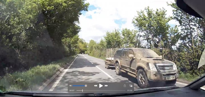 The "S**t Driving Caught On Cam" Thread (Vol 5) - Page 318 - General Gassing - PistonHeads UK - The image is a still photo taken from the interior of a vehicle. It captures a scene outside through the car's windshield, showing an overcast day with a muddy road ahead. On this road, there is a pickup truck partially obscured by a spray of water or mud, which suggests that the road conditions are poor due to recent rainfall or construction work. The road curves to the left in the distance, and there is vegetation on both sides of the vehicle. The photo appears to have been taken with a smartphone given its quality and composition, with the device's interface visible at the bottom.