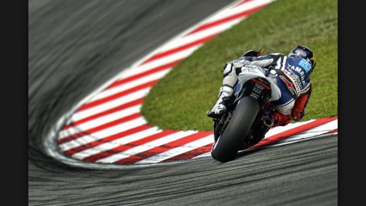 Fantastic Motorsport Photos! - Page 203 - General Motorsport - PistonHeads - This image captures a skilled motorcycle racer in the midst of executing a high-speed turn around a race track. The track features a prominent banked red and white curb, indicating that it is an important part of the racetrack. The rider, dressed in a complete racing suit, is leaning into the curve with his body positioned accurately to maintain control and speed. The wheels of the motorcycle are close to the track's edge, demonstrating the rider's precision and confidence in their abilities.