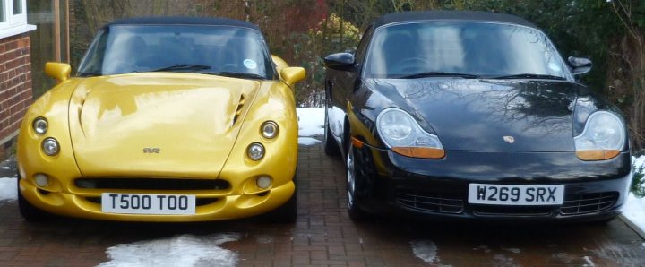 Votes please, which two to keep? - Page 1 - General Gassing - PistonHeads - The image showcases two luxury cars parked side by side on a brick driveway. They are compact in size, with a yellow convertible on the left and a black Porsche on the right. The snowy background suggests a cold or winter climate. The cars have personalized license plates. The driveway is graced with the shadows of the cars, adding depth to the scene. The vehicles are parked in front of a house, indicating a residential setting.