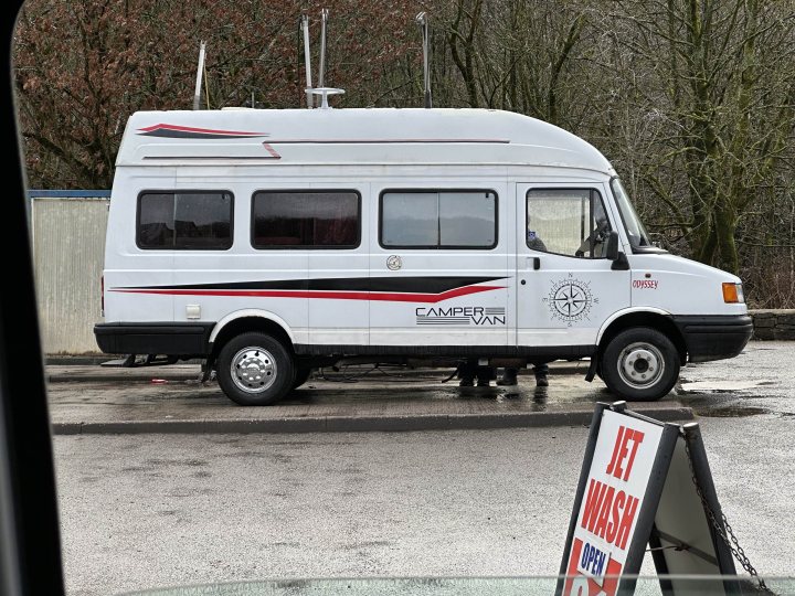 These pictures make my teeth itch - Page 361 - The Lounge - PistonHeads UK - The image shows a white and red camper van parked in an outdoor area. It has a pop-up top with windows, likely for sleeping or observation. The vehicle is marked with the logo of "Cambrian Explorer" and there are two visible antennas on the roof, which might be used for communication or entertainment purposes. The license plate is clearly visible, and a small sign on the side appears to read "WASH", indicating that it's a designated area for washing vehicles. In the background, you can see a building with a large window, suggesting that this could be in a commercial or industrial area. The overall setting suggests that the van may have been used for a trip and is now parked before being cleaned.