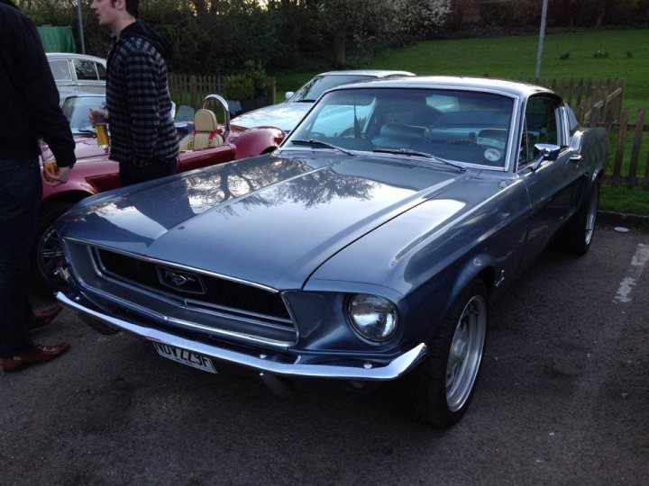 A car is parked on the side of the road - Pistonheads - The image showcases a classic Mustang car parked in a lot. The car is a striking blue model with black accents. It's parked close to other cars, suggesting a public parking area or event. The interior of the car is not visible, but the hood is propped open, revealing a polished engine. A person is standing near the car, possibly admiring it or waiting to access it later. The car's position and the open hood indicate that it might be undergoing a show or display, attracting positive attention from passersby or enthusiasts.