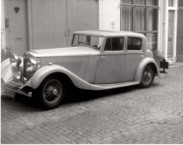 B&W Bentleys.... - Page 1 - Rolls Royce & Bentley - PistonHeads - This black-and-white photograph captures a **vintage car** parked on a **brick street** in **front of a building**. The car is a **classic model** with a long nose and a chrome hood, adding to its **nostalgic charm**. The setting appears to be quiet and calm, with no other vehicles or people visible, giving the viewer a sense of tranquility.